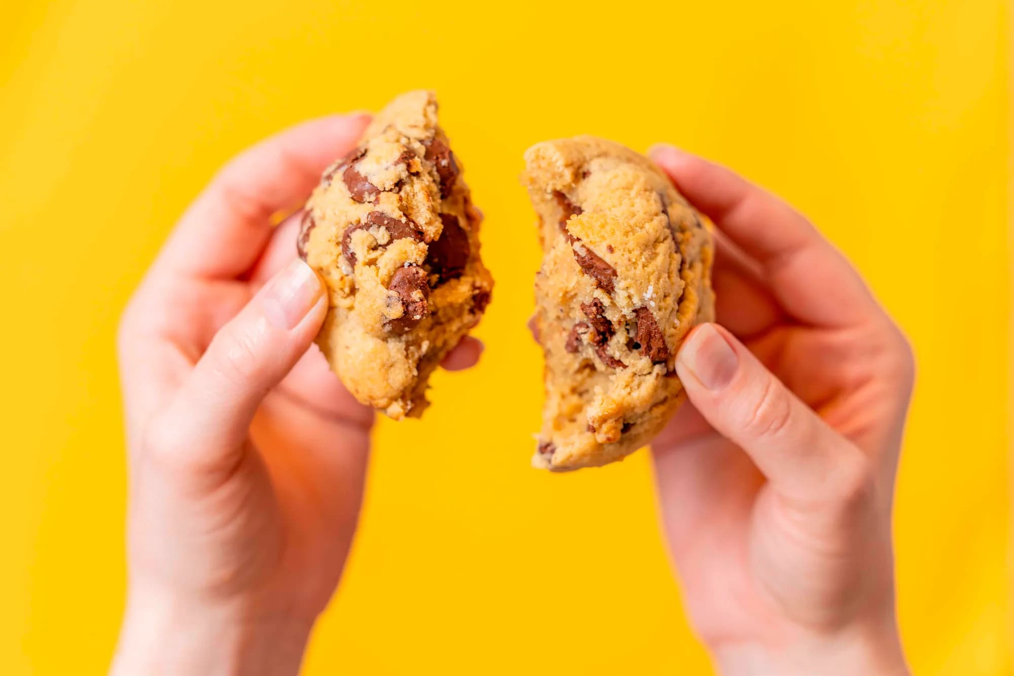 Two hands breaking a six-ounce cookie in half